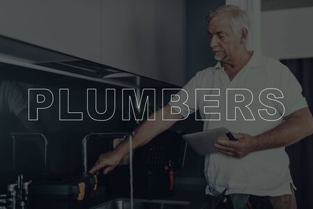 Old Gray Haired Man Working. Man is Plumber. Worker Located in a Modern Kitchen. Man Wearing in a White T-Shirt.の写真素材
