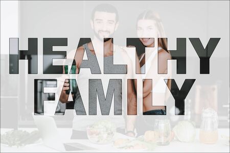 Healthy Family. Couple in Kitchen. Vegetables and Fruits on Table. Laptop on Table. Man Holding a Vegetable Cocktail.の写真素材