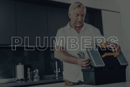 Old Gray Haired Man Posing. Man is Plumber. Worker is Taking Wrench from Tool Box. Tool Box on Table. Plumber Wearing White T-Shirt.の写真素材