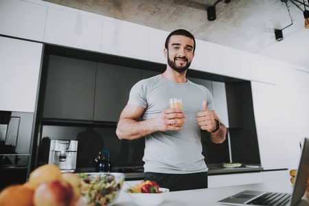 Athletic Man Stands In Kitchen. Posing Concept. Healthy Lifestyle. Young And Handsome. Sport Body. House Interior. Fruits And Vegetables. Morning Fresh Nutrition. Role Model. Thumbs Up.の写真素材