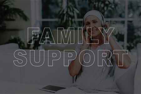 Family Support. Sick Mature Woman Sitting on Sofa. Smiling Sick Woman Listening Music in Headphones by Using Digital Tablet. Patient with Cancer in Hospital. Healthcare, Recovery and Sickness Conceptの写真素材