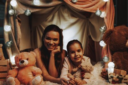 Mother and Daughter Lying on Carpet. Persons is Lying Under the Fake Tent. Daughter is Holding the Teddy Bears.の写真素材
