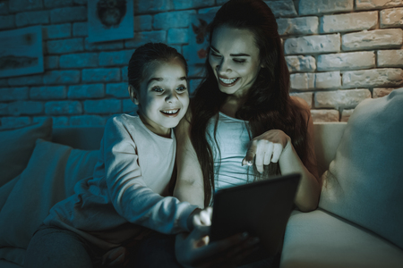 Mother with Daughter is Sitting on Couch. People Watching a Video on Tablet PC.の写真素材