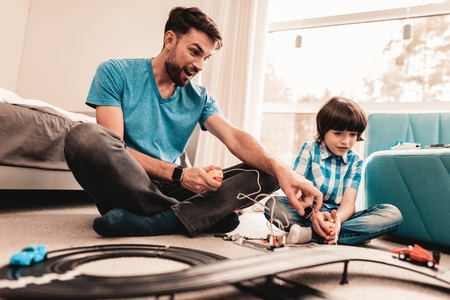 Bearded Father and Son Playing with Toy Race Road. Man Sitting on Floor.の写真素材