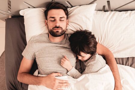 Little Son with Tired Sleeping Father in Bed. Family in Morning. Happy Family Concept.の写真素材