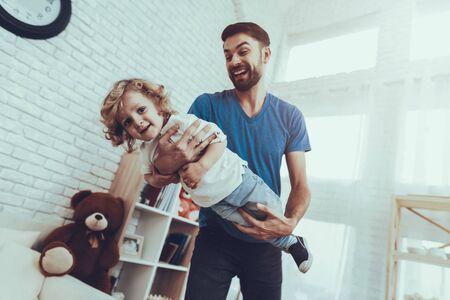 Man Spends Time with His Son. Father of Boy is Engaged in Raising Child. Father and Son is Playing. Man is Holding a Boy Like a Airplane. Persons is Smiling. People is Located in Bedroom.の写真素材