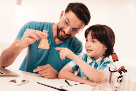 Youn Bearded Father Teaching Son in Shirt at Home. Education at Home. Using Microscope. Studding Chemistry. White Table in Room. Sitting Boy. Young Father. Lesson at Home. Education Concept.の写真素材