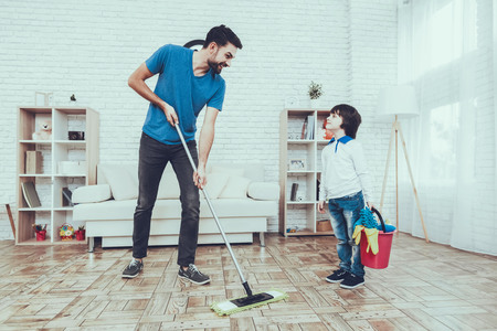 Man Spends Time with His Son. Father of Boy is Engaged in Raising Child. Father is Teaching a Son a Cleaning. Father and Son Washing the Floor with Mop. People is Located in Bedroom.の写真素材