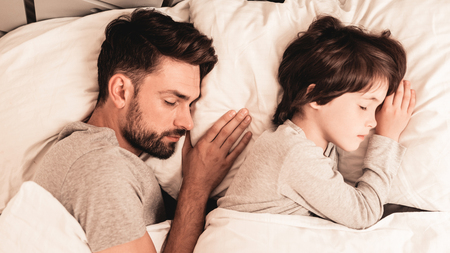 Little Son with Tired Sleeping Father in Bed. Family in Morning. Happy Family Concept. White Bed in Room. Father and Son at Home. Morning Routine. Lying in Bed. Sleeping Man. Blanket and Pillows.の写真素材