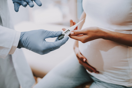 Pregnant Girl at the Gynecologist Doctor. Doctor is a Young Man. Doctor and Woman is Holding the Pregnancy Test. Girl is Sitting on Couch. People is Located at Clinic. Closeup View.の写真素材
