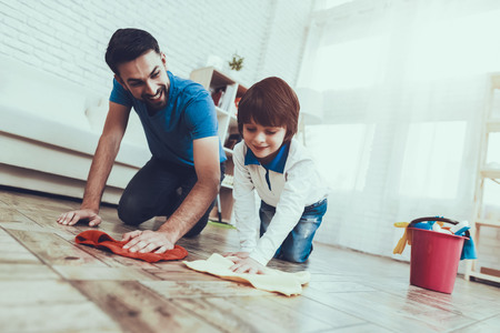 Man Spends Time with His Son. Father is Engaged in Raising Child. Father is Teaching a Son a Cleaning. Father and Son Washing the Floor with Rags. Persons is Smiling. People is Located in Bedroom.の写真素材