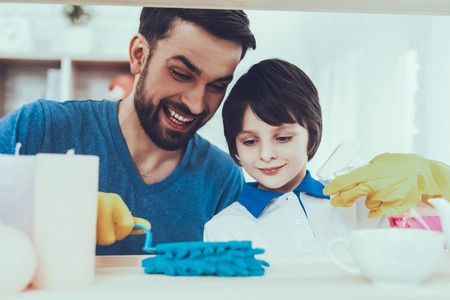 Man Spends Time with His Son. Father of Boy is Engaged in Raising Child. Father is Teaching a Son a Cleaning. Father and Son Wipe the Furniture Surfaces from Dust. People is Located in Bedroom.の写真素材
