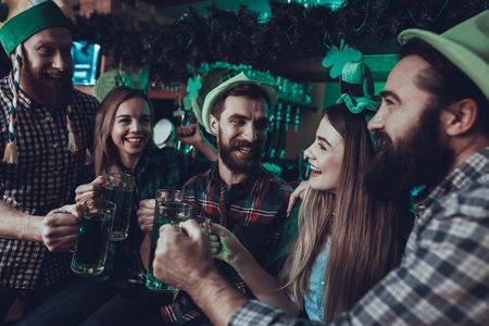 Saint Patrick's Day Party. Group of Friends is Toast and Drinking a Green Beer. Friends is a Young Men and Women. People Wearing a Green Hats. People is Happy and Smiling. Pub Interior.の写真素材
