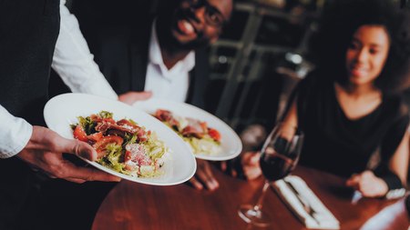 Waiter Serving Salad to African Couple Restaurant. Romantic African American Couple in Love Dating. Cheerful Man and Woman Drinking Red Wine. Romantic Concept. Anniversary. Glasses of Red Wine.の写真素材