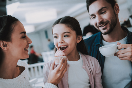 Family Resting in Cafe. Family is a Mother, Father and Daughter. People is Eating a Cakes and Drinking a Tea. Persons is Sitting at Table. People is Happy and Smiling. Sunny Daytime.の写真素材