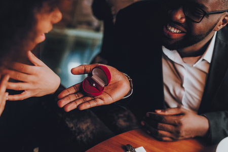 African Handsome Man Proposing to Girlfriend. Romantic Couple in Love Dating. Cutel Man and Girl in a Restaurant. Romantic Concept. Surprised Attractive Woman Getting a Marriage Proposal.の写真素材