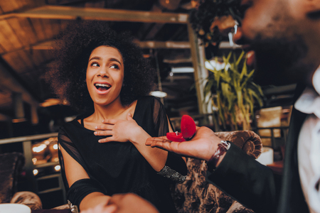 African Handsome Man Proposing to Girlfriend. Romantic Couple in Love Dating. Cutel Man and Girl in a Restaurant. Romantic Concept. Surprised Attractive Woman Getting a Marriage Proposal.の写真素材