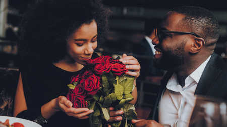 African American Couple Dating in Restaurant. Romantic Couple in Love Dating. Cutel Man and Girl in a Restaurant Making Order. Romantic Concept. Man Giving Bouquet of Flowers. Red Roses.の写真素材