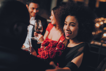Friends in a Restaurant Enjoying Romantic Evening. Group Happy Friends Enjoying Dating in Restaurant. Double Couple Dating in Restaurant. Romantic Concept. Bouquet Red Roses. Love Concept.の写真素材