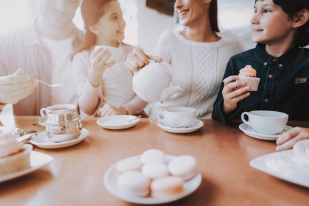 Family Resting in Cafe. Family is a Mother, Father, Daughter and Son. People is Eating Cakes and Drinking a Tea. Persons is Sitting at Table. People is Happy and Smiling. Sunny Daytime.の写真素材