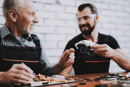 Two Men Repairing Hardware Equipment in Workshop. Repair Shop. Worker with Tools. Computer Hardware. Young and Old Workers. Modern Devices. Digital Device. Laptop on Desk. Electronic Devices Concept.の写真素材