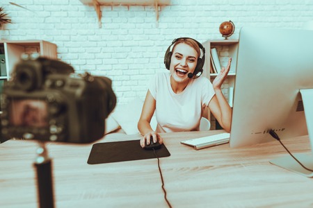 Blogger Makes a Video. Blogger is Gamer. Blogger is Young Smiling Woman. Camera Shoots a Video. Woman in Headphones Playing a Video Game on Computer. Woman Looking into a Camera. Studio Interior.の写真素材