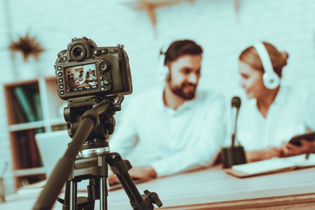 Blur Image of Bloggers Makes a Video. Bloggers is Smiling Man and Woman. Camera Shoots a Video. People Wearing a Headphones. Persons is Talking at Microphone. People in Studio Interior.の写真素材