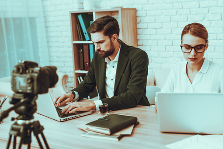 Bloggers Makes a Video. Bloggers is Young Smiling Man and Woman. Video About a Business. Camera Shoots a Video. Supplies on Table. People is Using a Laptops. People in Studio Interior.の写真素材