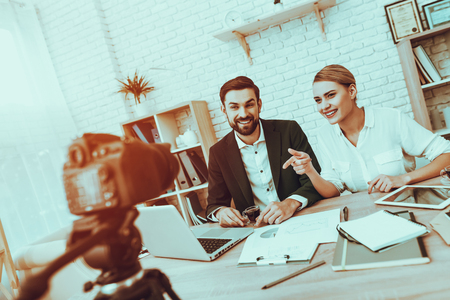 Bloggers Makes a Video. Bloggers is Young Smiling Man and Woman. Video About a Business. Camera Shoots a Video. Gadgets and Supplies on Table. People Looking into a Camera. People in Studio Interior.の写真素材