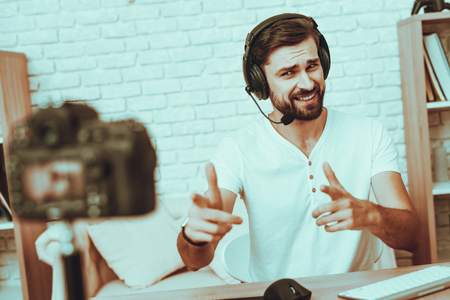 Blogger Makes a Video. Blogger is Gamer. Blogger is Young Beard Man. Camera Shoots a Video. Man in Headphones Playing a Video Game on Computer. Man Looking and Pointing into a Camera. Studio Interior.の写真素材