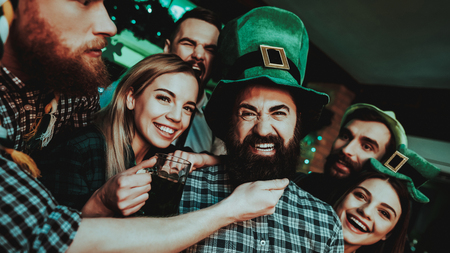 Black Bearded Man With Company. St Patrick's Day. Bar Counter. Alcohol Handling. Smiling Teenagers. Good Festive Mood. Bright Lights. Funny Club Visitors. Celebrating Together. Night Party.の写真素材