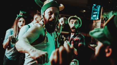 Two Men Fight In Pub. Saint Patrick's Day Concept. Punch In The Face. Quarrel In The Bar. White Singlet. Agressive Males. Angry Guys. Violence In The Club. Funny Hats. Bright Lights.の写真素材