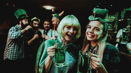 Two Girls In Carnival Clothes. St Patrick's Day Celebrating Concept. Bar Counter. Good Festive Mood. Bright Lights. Club Visitors. Having Fun. Resting Together. Drinking Beer From Glass.の写真素材