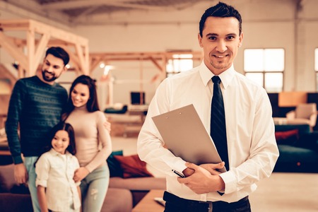 Young Family Consulting With Furniture Seller. Happy Together. Bright Office. Sunny Day.Manager In Shirt And Tie. Business Meeting. Room Interior. Parents And Daughter. Look Around The Store.の写真素材