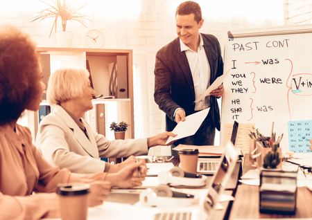 Pupils Studying a English Language. Teacher is Giving Back a Test to Student. Students is Multiracial People of Different Ages. Students is Sitting at Table. People Located in Classroom.の写真素材