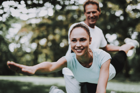 Young Couple in Sportswear Doing Yoga in Park. Sport and Healthcare Concept. Young Man Outdoor. Trainer in Summer Park. Smiling Young Woman.の写真素材