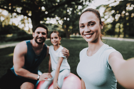 Happy Young Family Using Tablet in Summer Park. Sport and Healthcare Concept. Summer Park.Father and Mother. Smiling Daughter. Using Digital Device.の写真素材