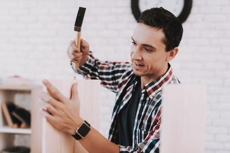Young Man Assembling Wooden Bookshelf at Home. Wooden Bookcase. Selfmade Furniture. Man and Hobby. White Room. Engineer with Tool. Young Man at Home.の写真素材