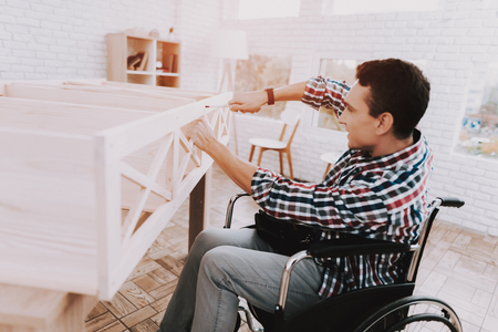 Young Man on Wheelchair Assembling Wooden Bookshelf at Home.の写真素材