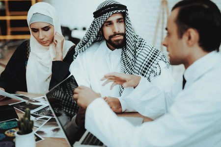 Male Doctor Consulting Arabic Family at Hospital. Doctor Explaining Diagnosis with Laptop. Consultation at Clinic. Reception of Therapist. Discussing Diagnosis. Examination. Medical Concept.の写真素材