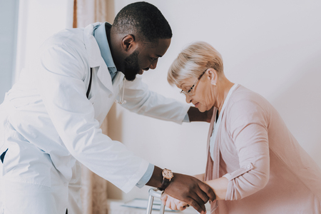 Doctor Helps Woman Get Up. Patient Feel Sick. Smiling Doctor. Doctor Examines Elderly Patient. Woman Tell about her Condition. Woman Try to Stand Up. Nursing Home. Doctor Interviews Woman.の写真素材