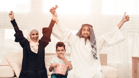 Happy Arabian Family Playing on Console at Home. Family Sitting on Sofa. Man Using Digital Device. Smiling Boay at Home. Muslim Family. Smiling Boy. Young Arabian Woman. Woman in Black Dress.の写真素材
