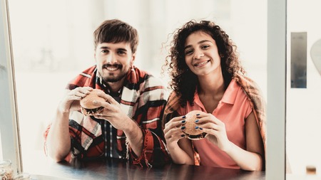 Young Couple in Checkered Plaids Eating Burgers. Street Food Concept. Food in Town. Selling Snacks. Girfriend and Boyfriend. Summer Day. Square in European City. Smiling People in Blanket.の写真素材
