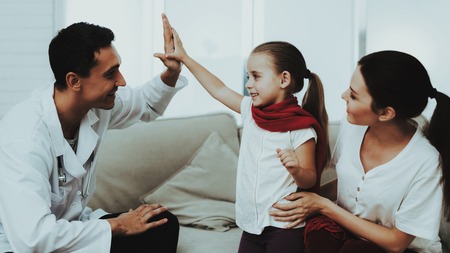 Doctor Visiting Little Girl in Red Scarf with Cold. Sick Young Girl. White Sofa in Room. Doctor in Uniform. Disease Concept. Healthcare and Healthy Lifestyle Concept. Mother with Daughter.の写真素材