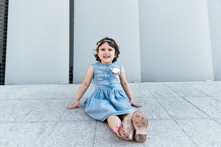 Adorable smiling little girl sitting near a grey wallの写真素材