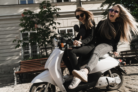 Young and beautiful girls in sunglasses riding a scooter. Portrait of pretty ladies riding a...
