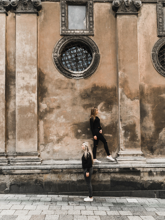 Attractive woman tourists in old european city. Beautiful young girls standing near the ancient stone house. Stylish teens traveling and enjoying summer time in Lviv, Ukraine. Girls in black enjoying summerの写真素材