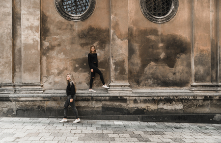 Attractive woman tourists in old european city. Beautiful young girls standing near the ancient stone house. Stylish teens traveling and enjoying summer time in Lviv, Ukraine. Girls in black enjoying summerの写真素材