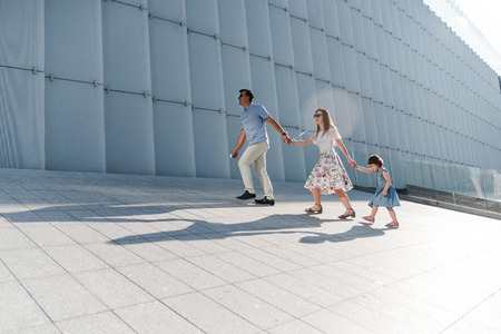 Young family with little daughter walking near the modern building in high-tech architecture style....