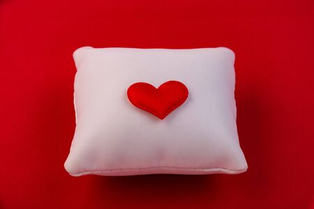 White pillow with a red heart in the center isolated on a red background.の写真素材
